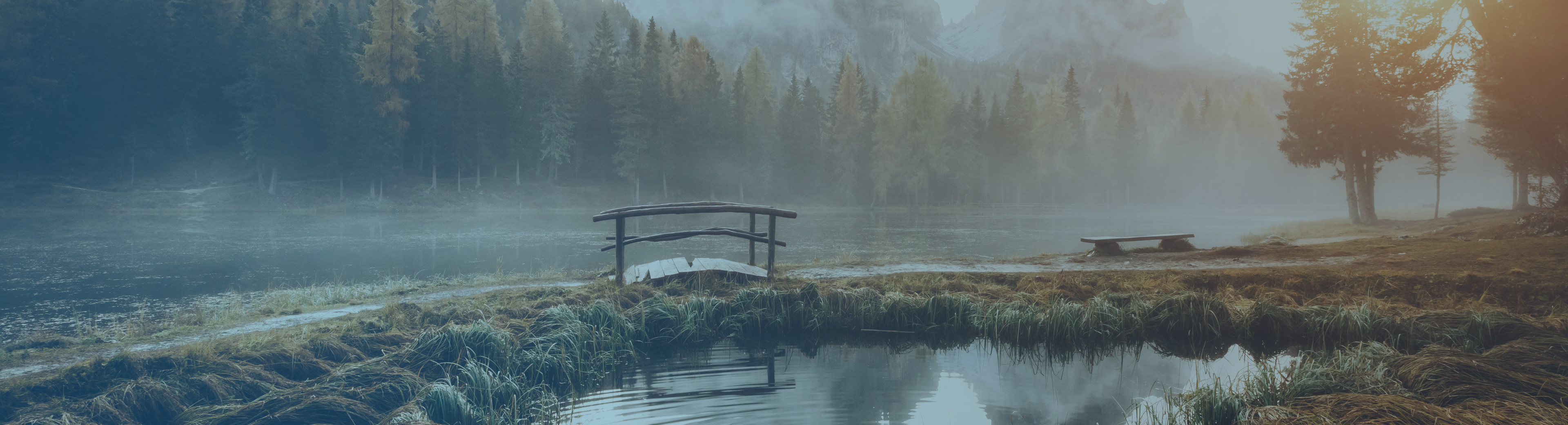Small footbridge with sun rising through the fog beyond